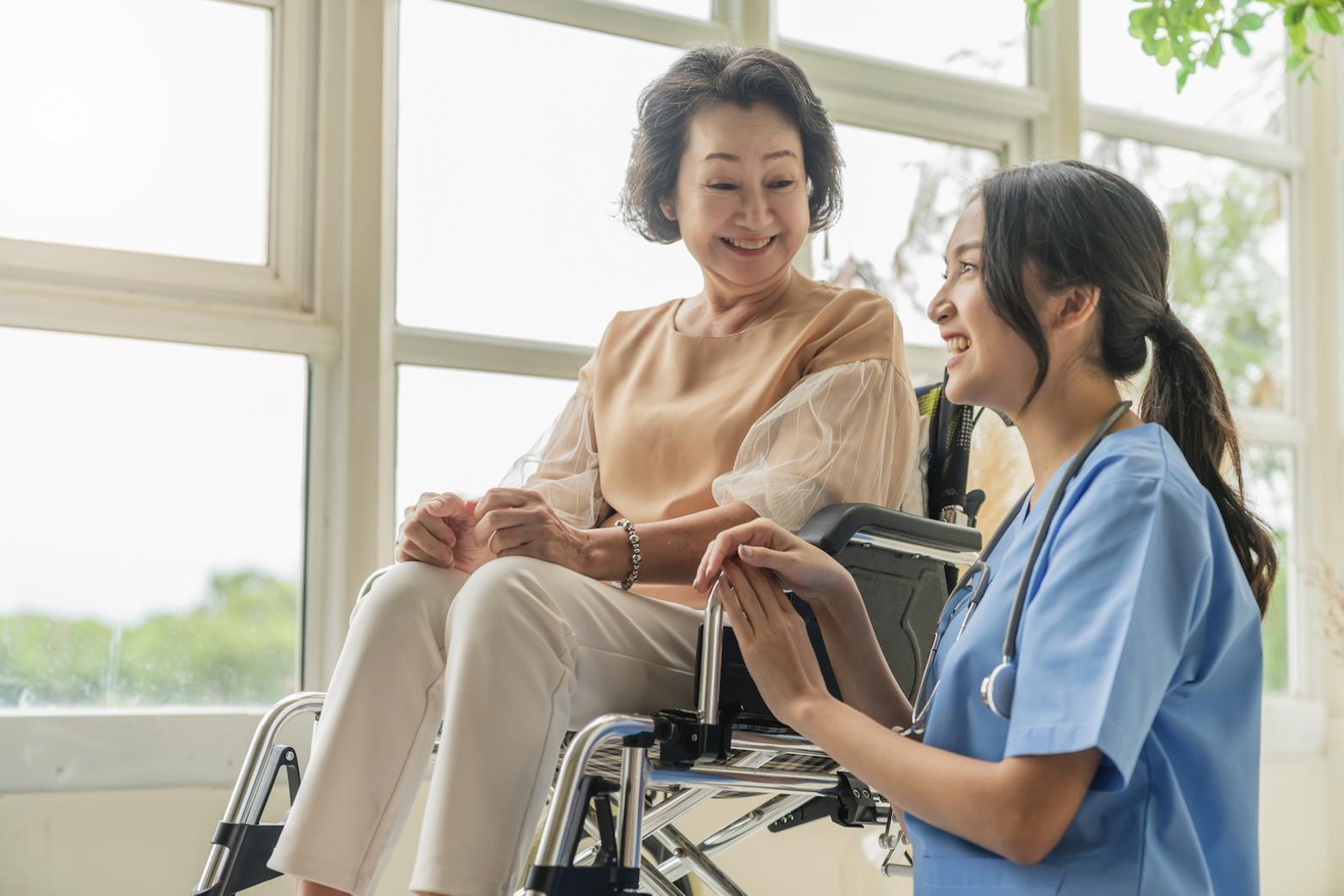 healthcare worker kneeling down next to a patient in a wheelchair